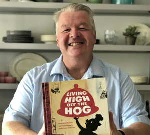 Chef Michael Olson smiling and holding his book, Living High Off the Hog