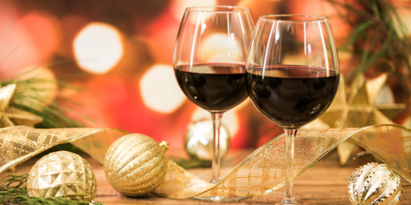 two red wine glasses in the foreground, blurry tree lights in the background.