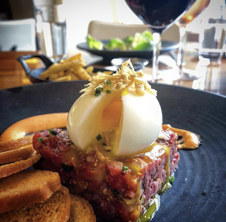 side view of steak tartare with soft boiled egg oozing overtop